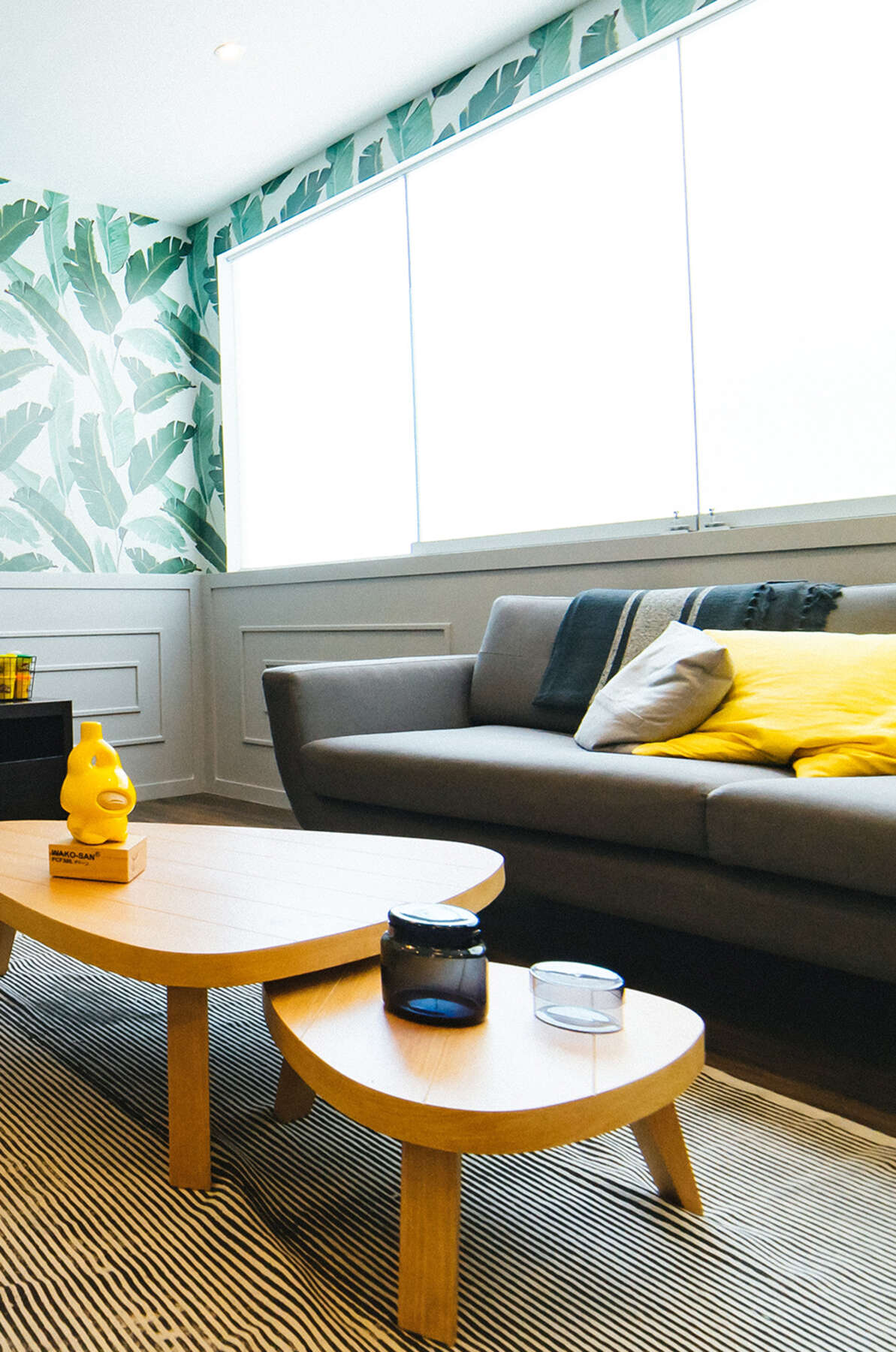 Office seating area with sofa, yellow pillows and wood coffee tables beneath large windows